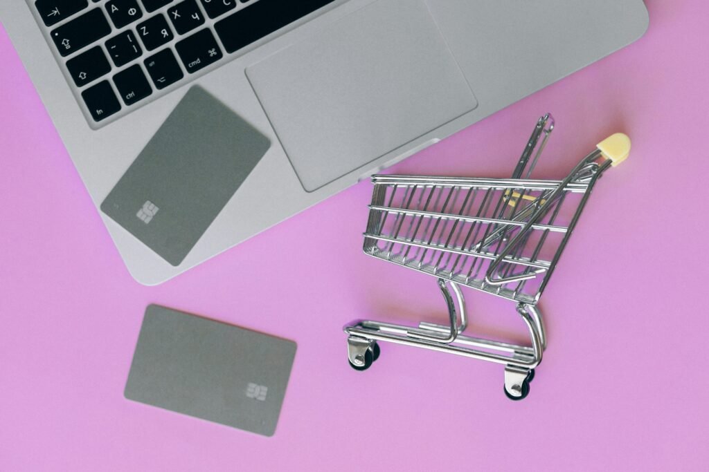 A minimalist flat lay of a credit card, laptop, and miniature shopping cart.